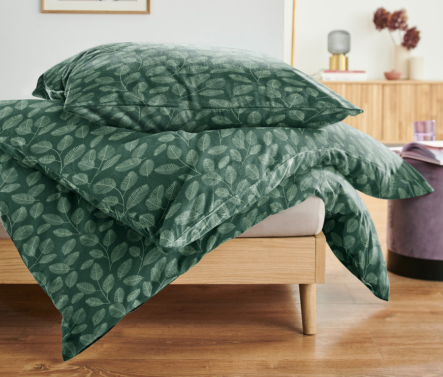 Une parure de lit en molleton verte de taille standard et grande taille avec un motif de feuilles est posée sur un lit.