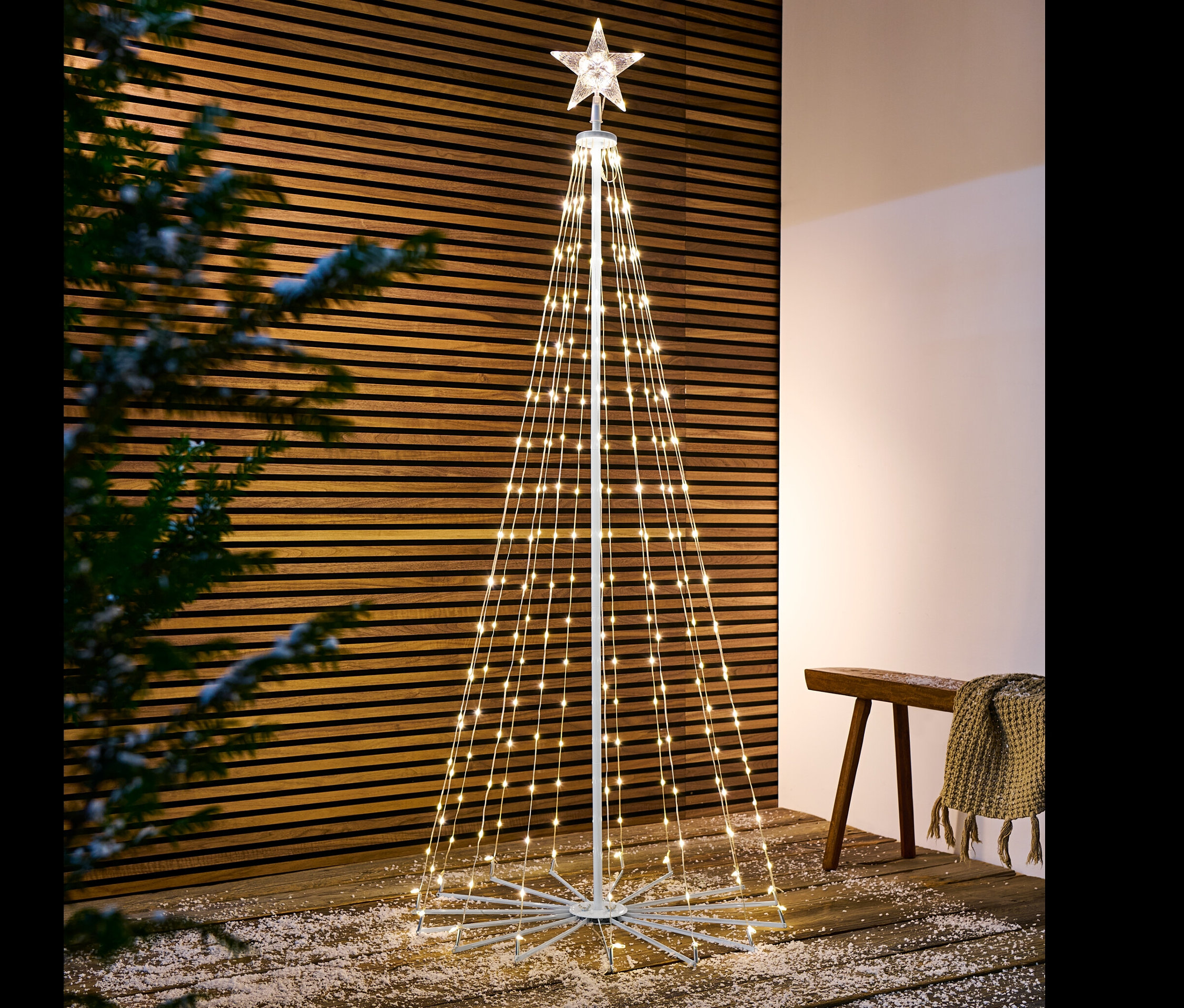 Un arbre à LED pliant se dresse sur un plancher en bois saupoudré de neige.