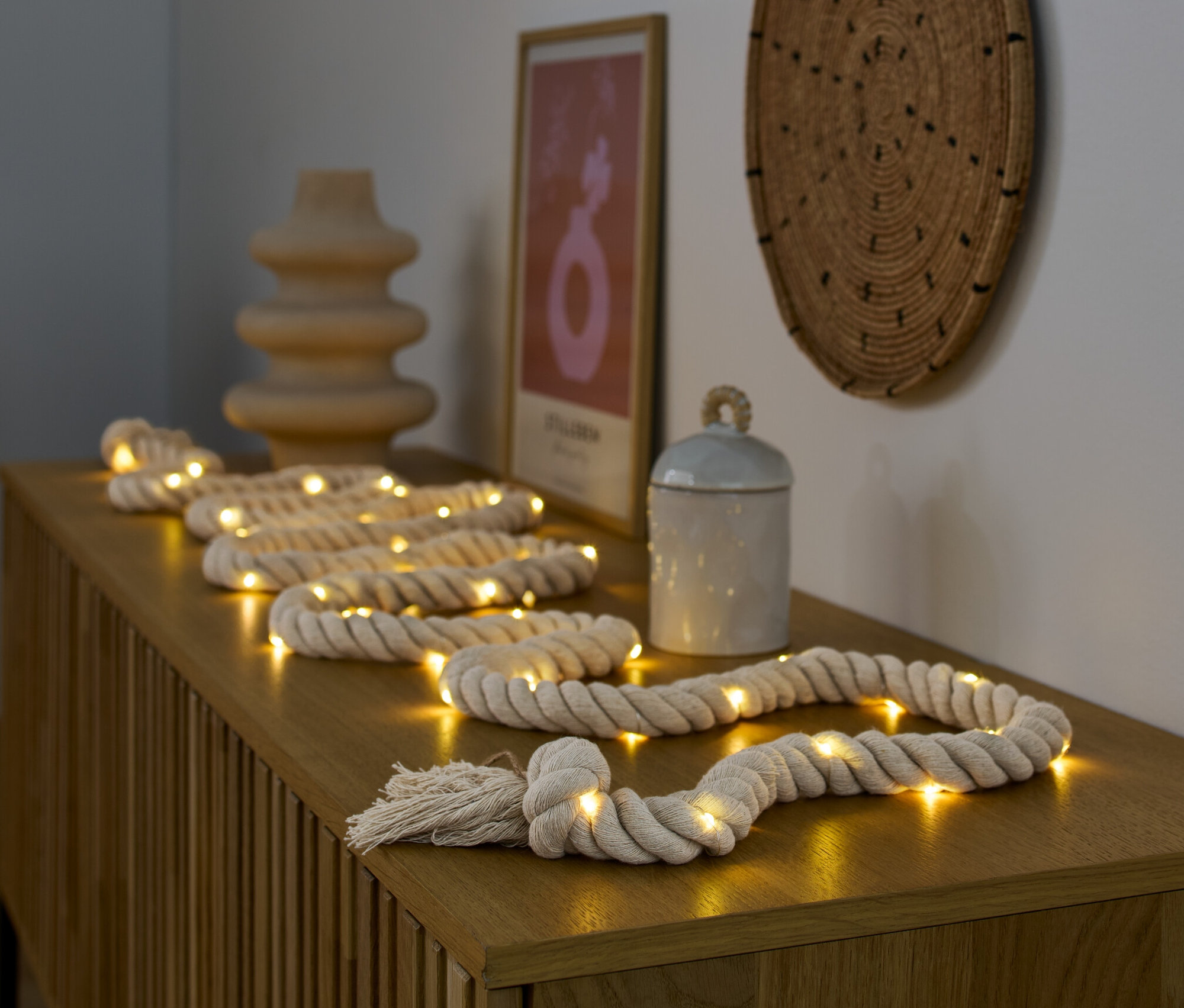 Guirlande lumineuse à LED « cordage » posée sur une commode en bois à côté d'un vase et d'une boîte.