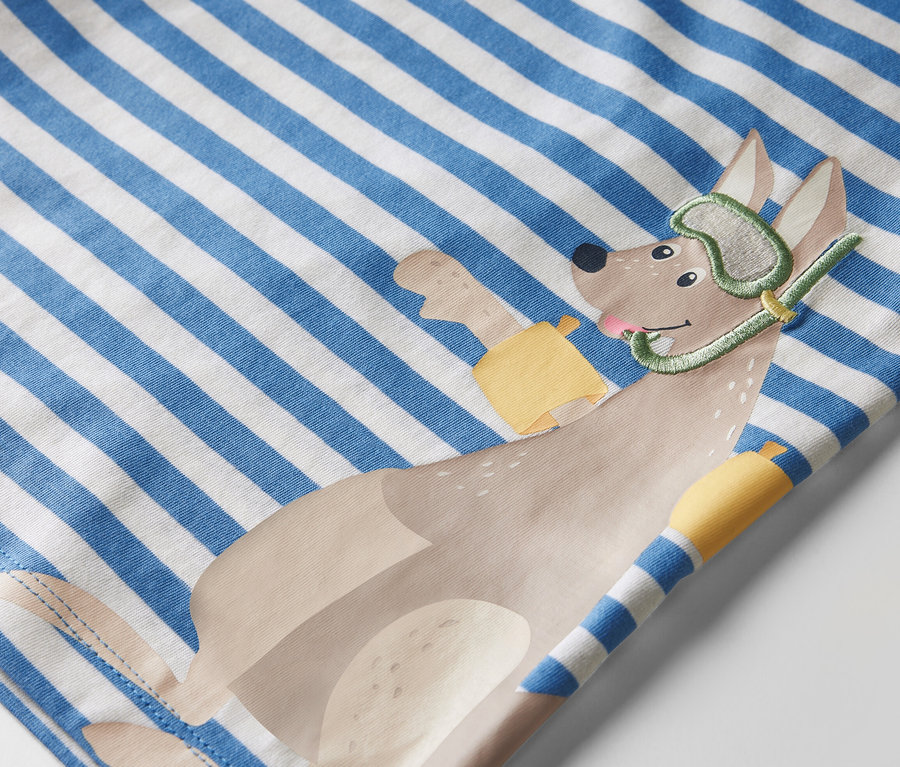 Gros plan sur un t-shirt pour enfant rayé bleu et blanc avec un motif appliqué représentant un chien portant un masque et un tuba de plongée.