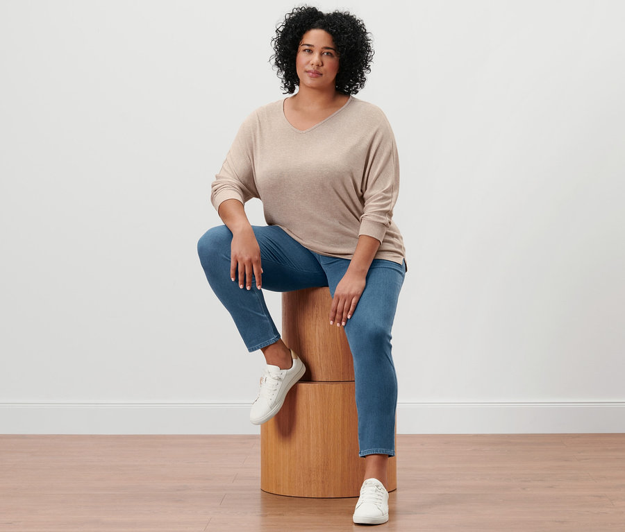 Une femme est assise sur un tabouret en bois et porte des baskets en cuir, un jegging et un t-shirt à manches chauve-souris.