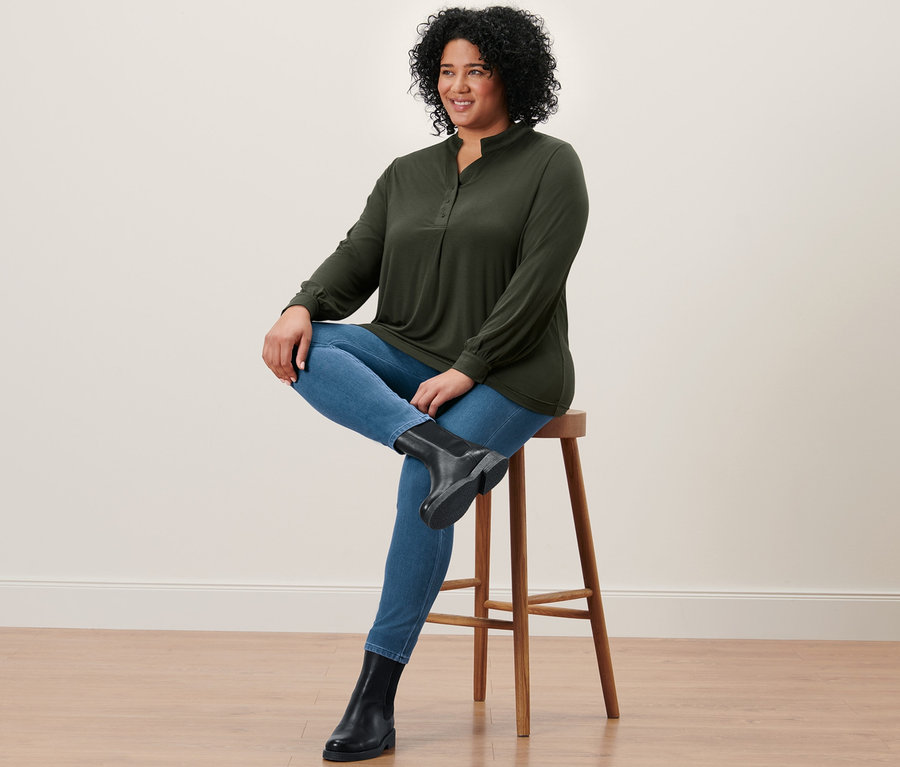 Femme assise sur un tabouret portant un jegging, des bottines en cuir et une blouse.