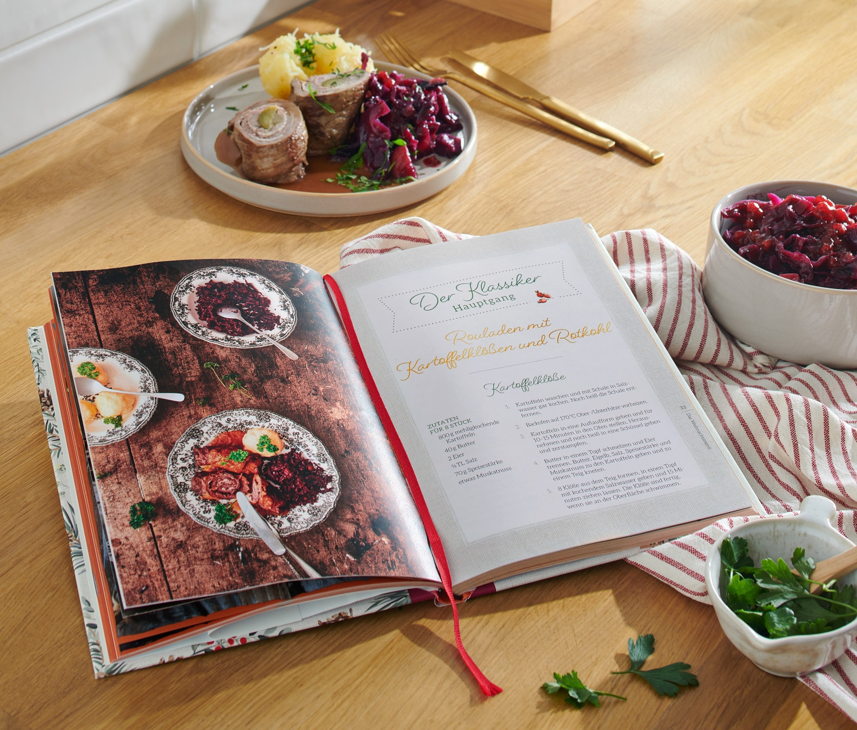 Livre de cuisine ouvert sur une table en bois avec des aliments dans des bols et sur une assiette, à côté le livre « Christmas is a feeling » (en allemand).