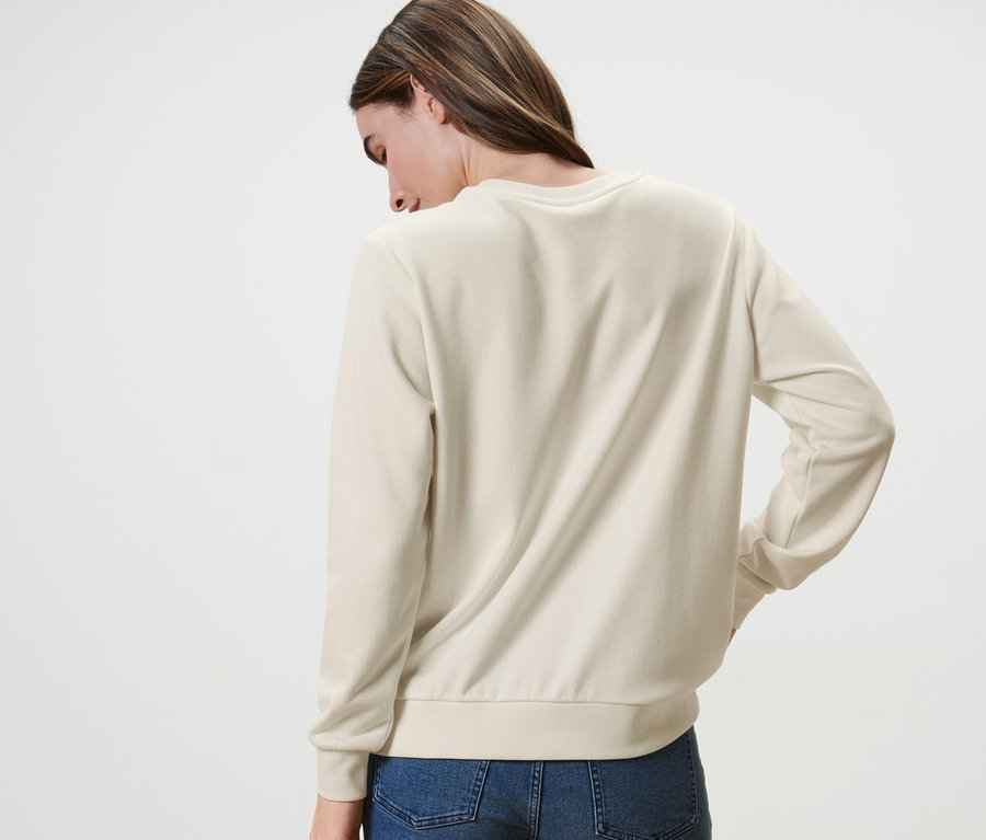 Une femme, dos à la caméra, porte un sweat-shirt avec broderie et un jean.