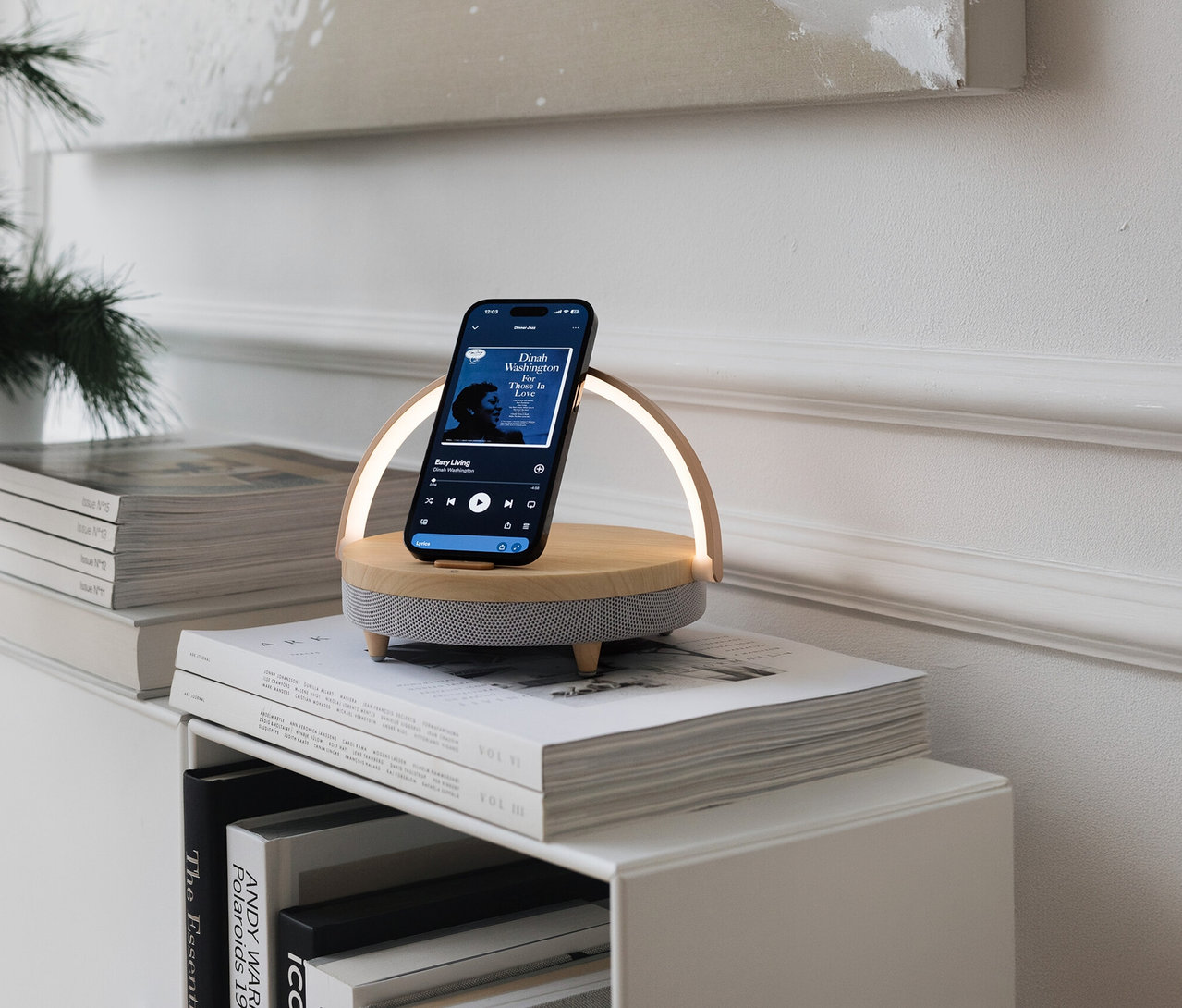 Téléphone sur enceinte Bluetooth® avec chargeur sans fil et veilleuse LED posée sur une pile de livres. Le téléphone affiche une application musicale.