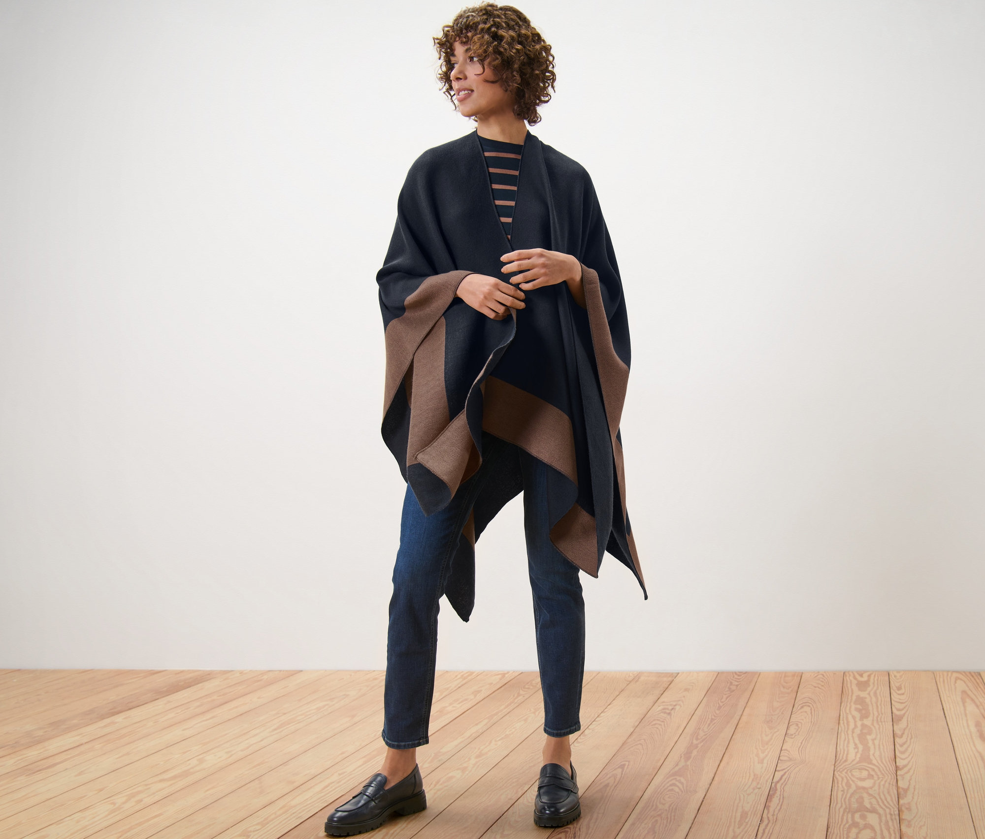 Une femme debout sur un plancher en bois porte un poncho tendance.