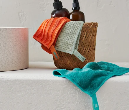 Lot de chiffons de nettoyage dans un panier en osier à côté de deux bouteilles marron.