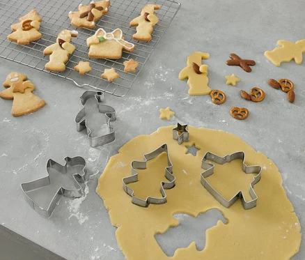 5 emporte-pièces pour biscuits sont posés sur un rouleau à pâtisserie et découpent des formes dans la pâte à biscuits.
