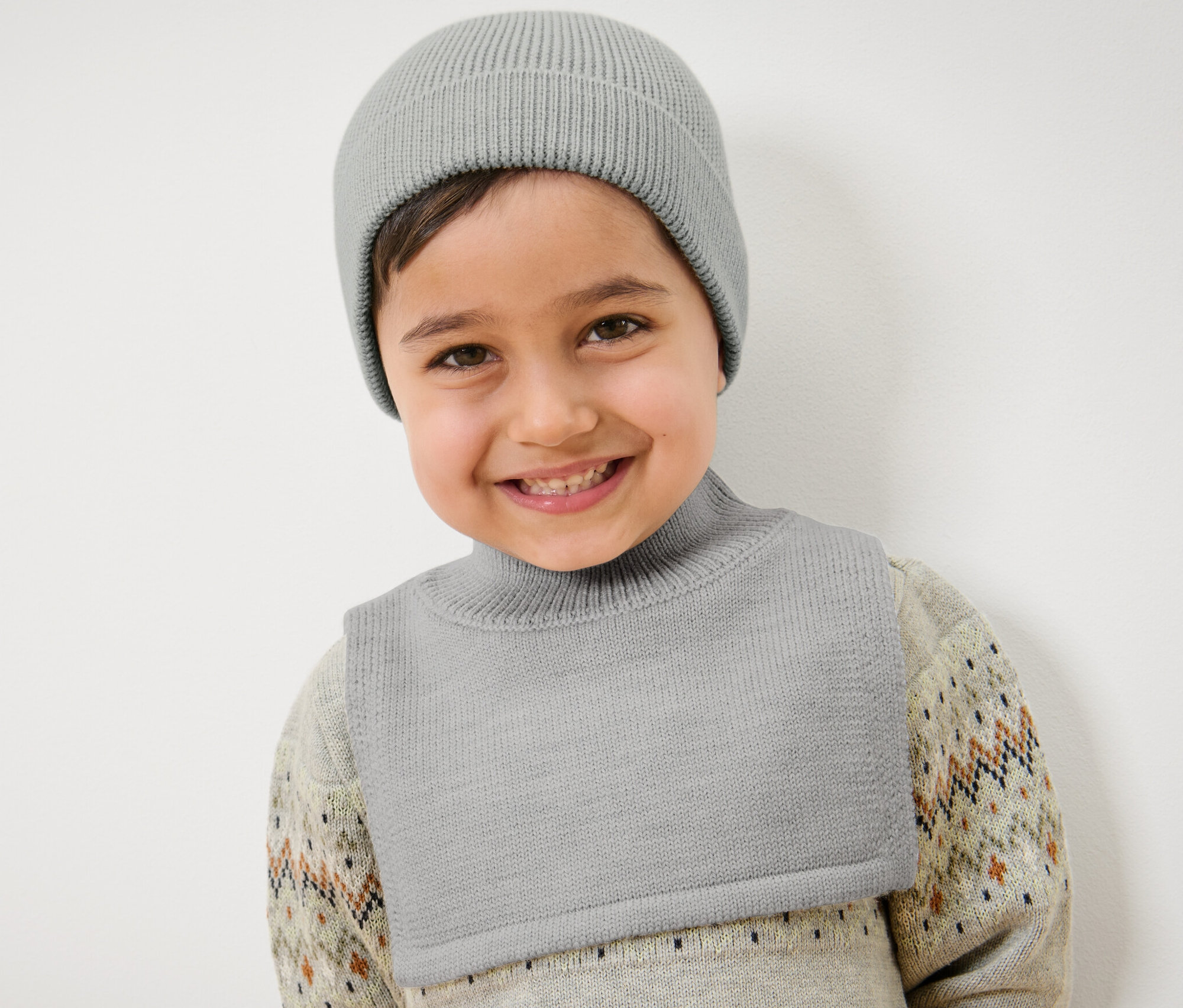Un enfant souriant porte un bonnet de laine en maille gris.