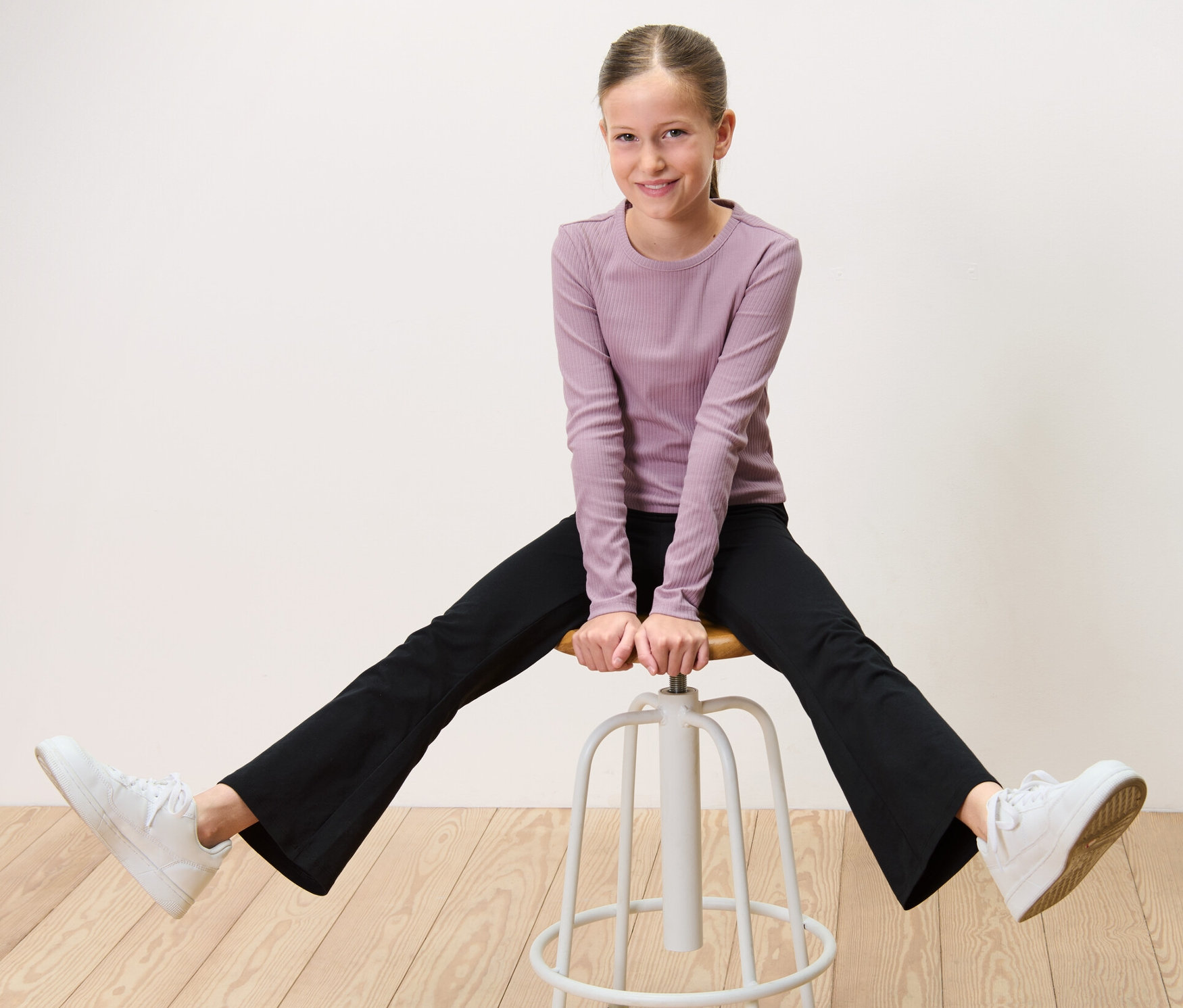 Une fille assise à califourchon sur un tabouret porte 2 leggings évasés pour enfant.