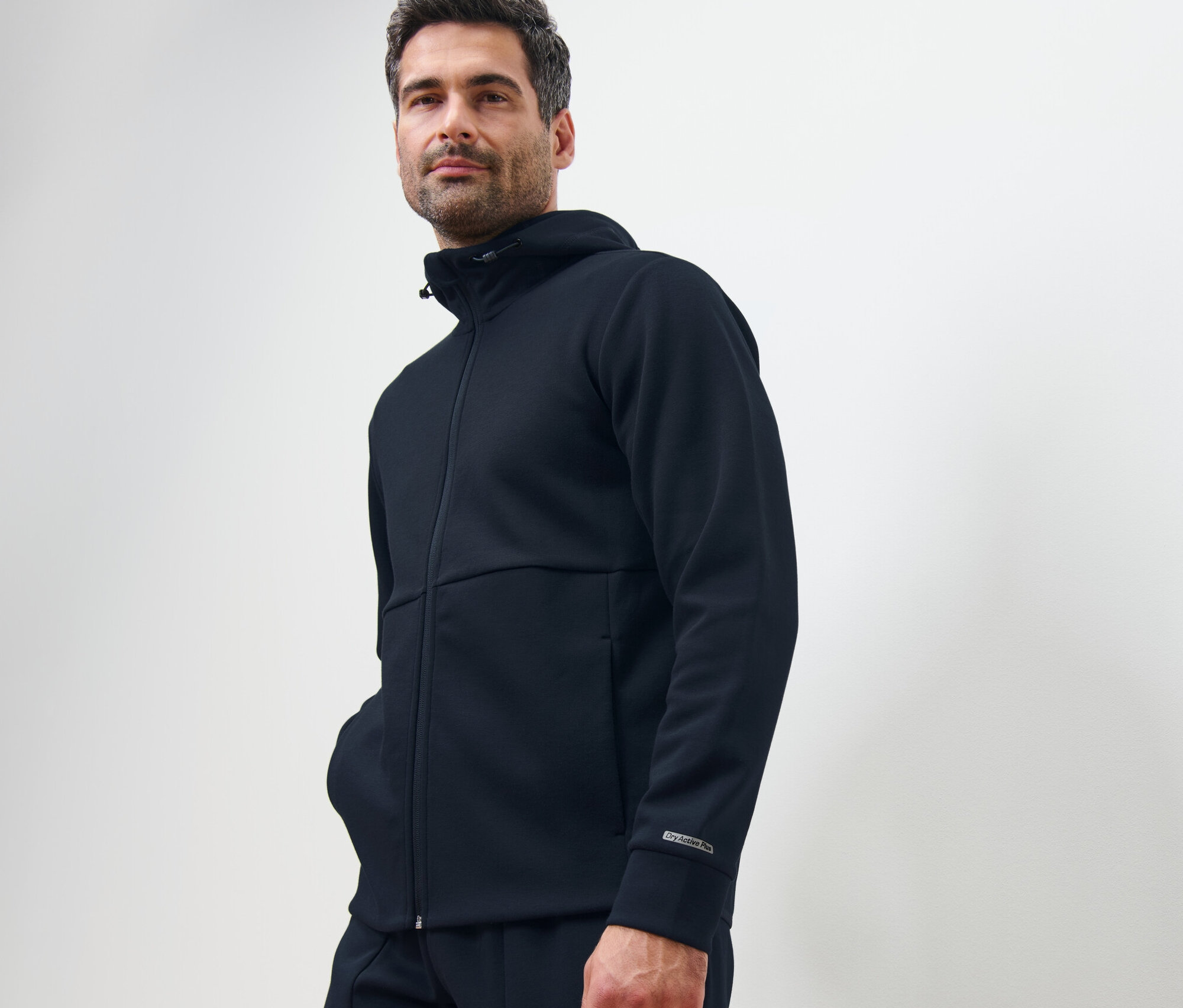 Un homme pose en veste technique en sweat bleu marine.