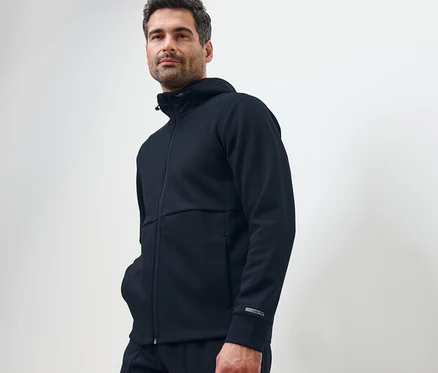 Un homme pose en veste technique en sweat bleu marine.