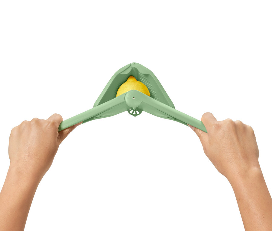 Deux mains pressent un presse-agrumes compact vert avec un citron à l'intérieur.