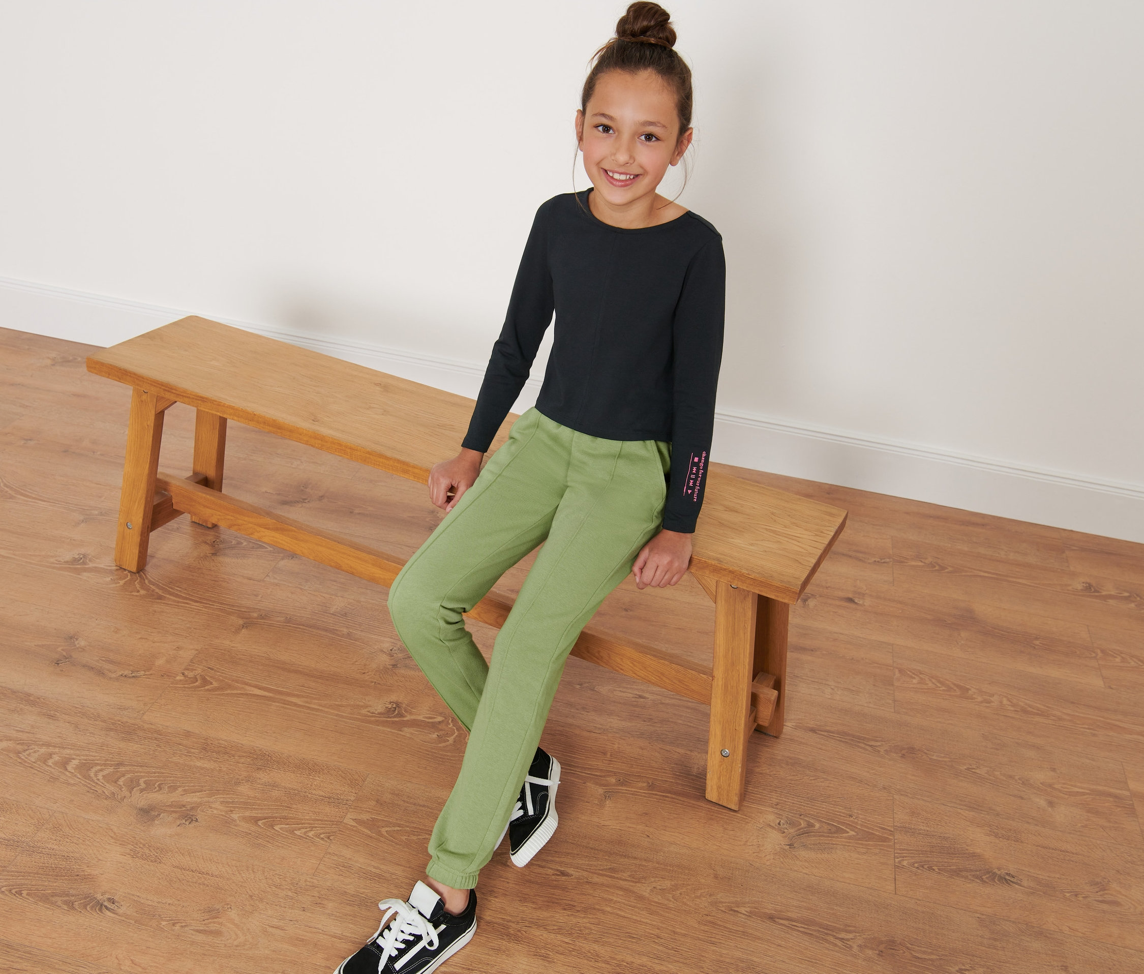 Une fille est assise sur un banc et porte un pantalon de survêtement pour enfant.