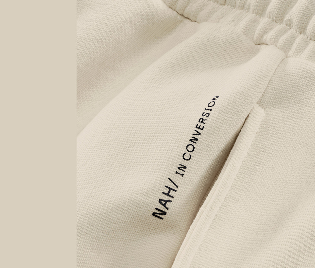 Détail d'un pantalon de jogging beige NAH/STUDIO en coton durable.