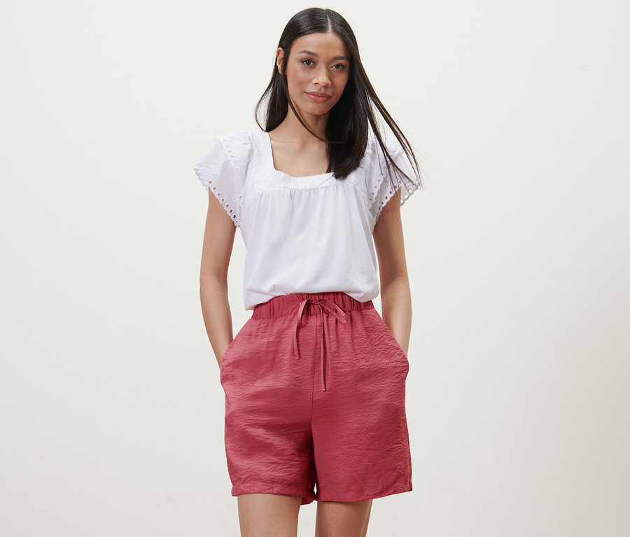 Femme posant en short framboise et chemisier blanc.