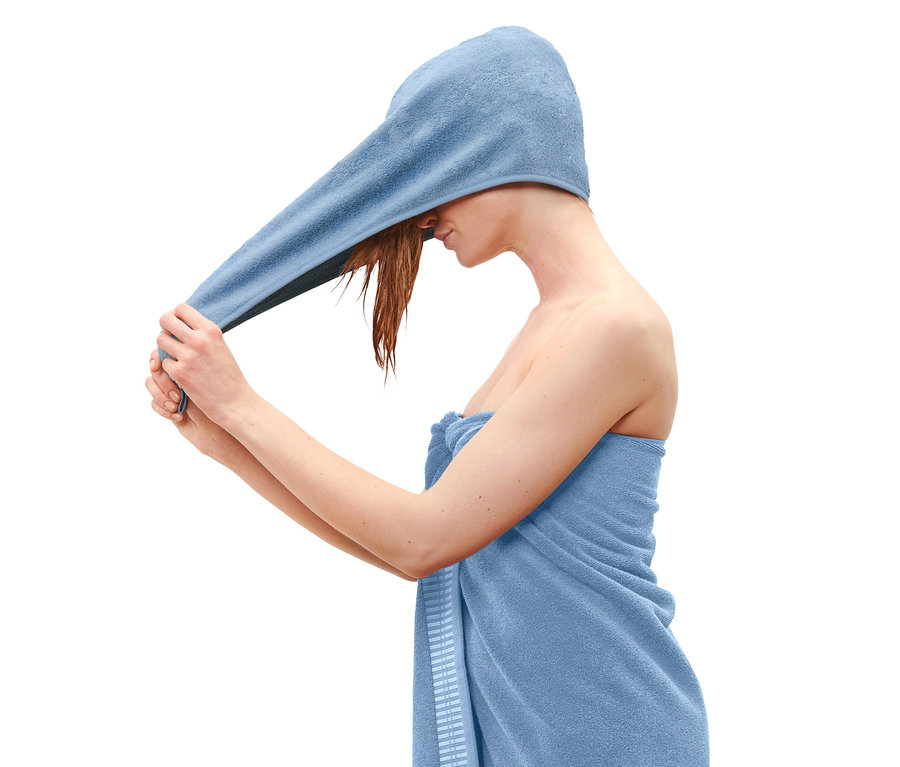 Une femme enroule une serviette turban bleue autour de sa tête.