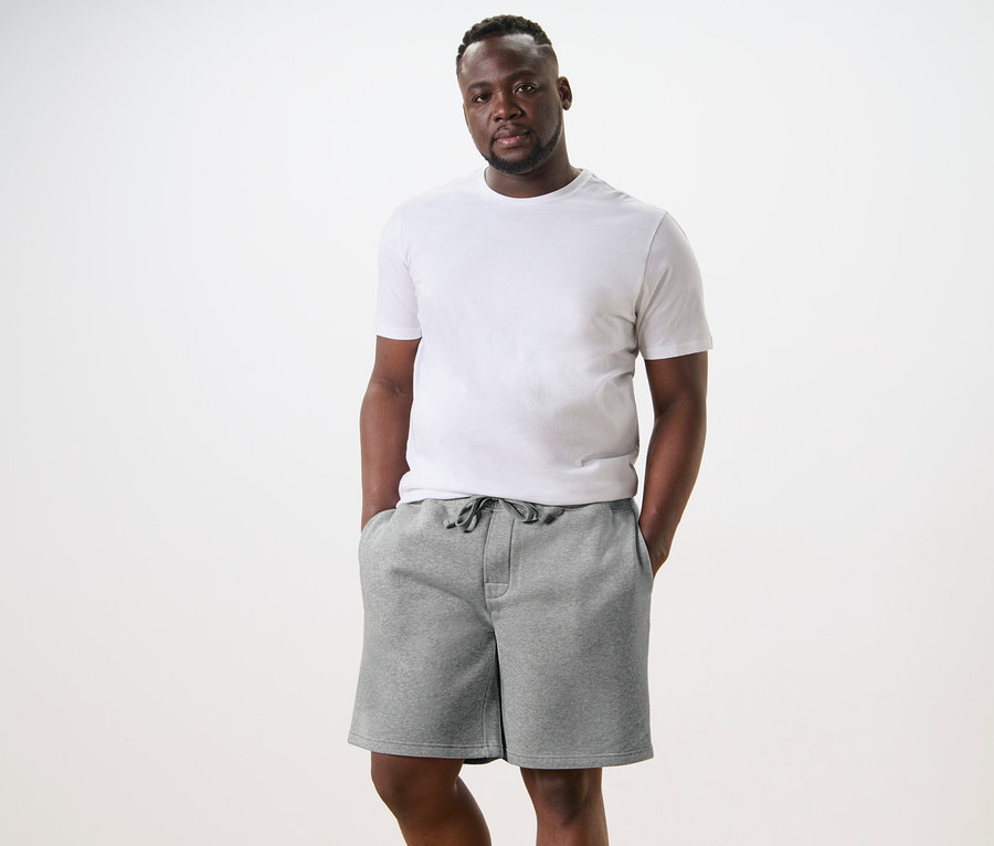 Un homme debout, les mains dans les poches d'un short en sweat gris clair.