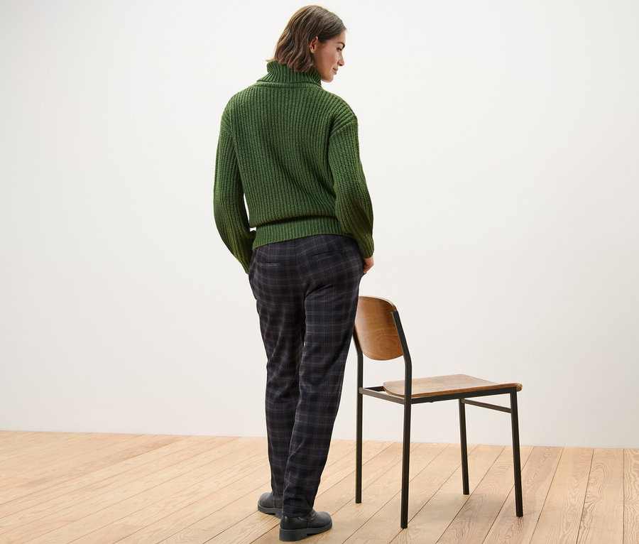 Une femme, vue de dos, porte un pull vert et un pantalon de jogging à carreaux.
