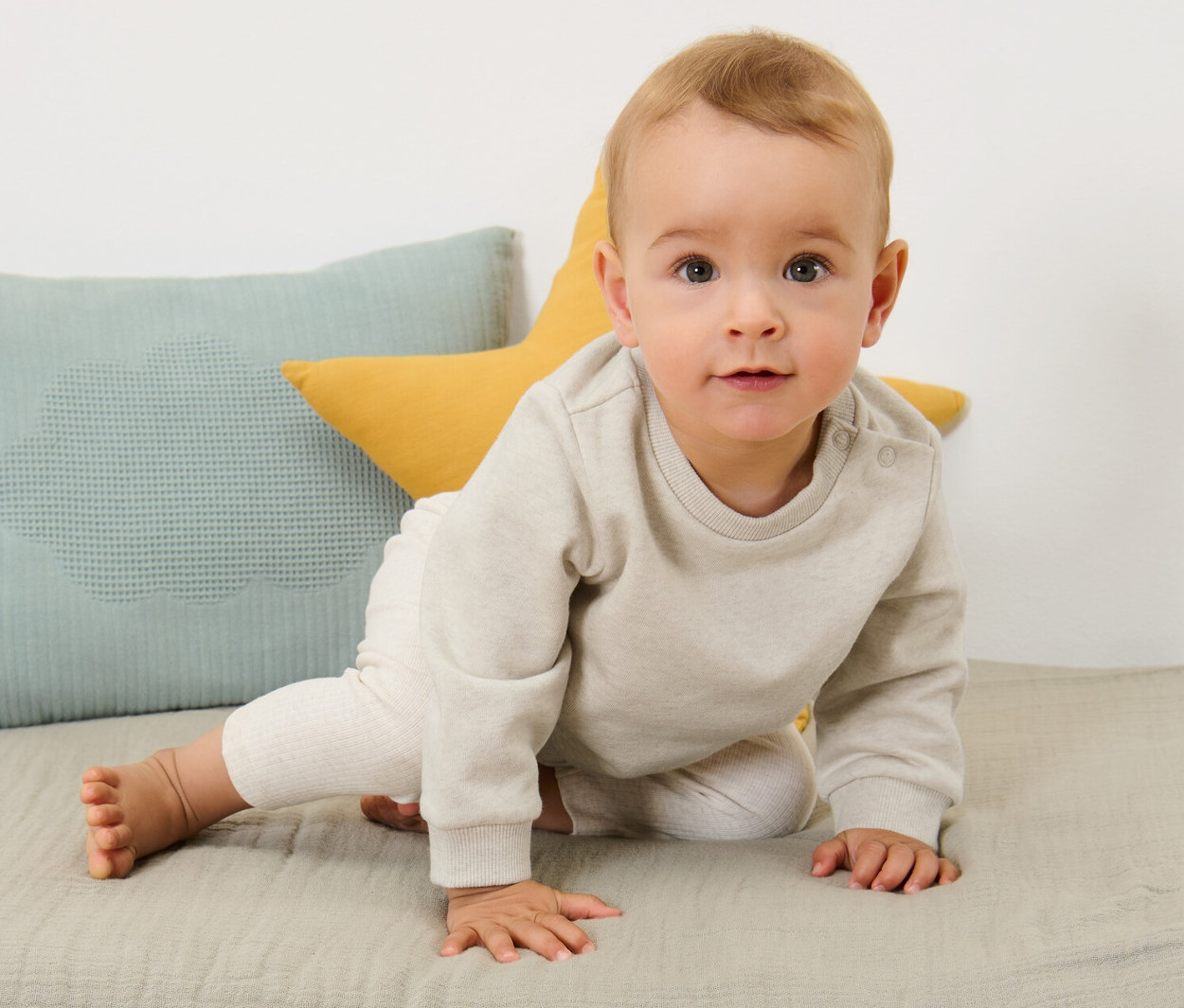 Un bébé rampe sur un tapis à côté de coussins. Il porte 2 sweatshirts pour bébé avec intérieur gratté.