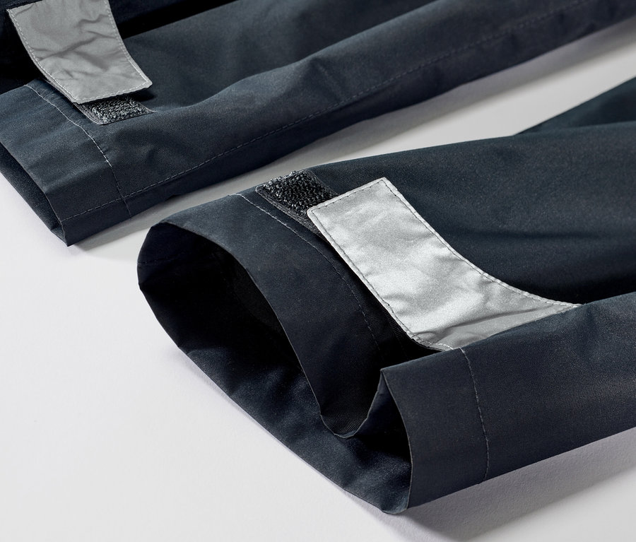 Gros plan sur un pantalon de pluie pour enfant avec des réflecteurs et une fermeture velcro à l'ourlet.