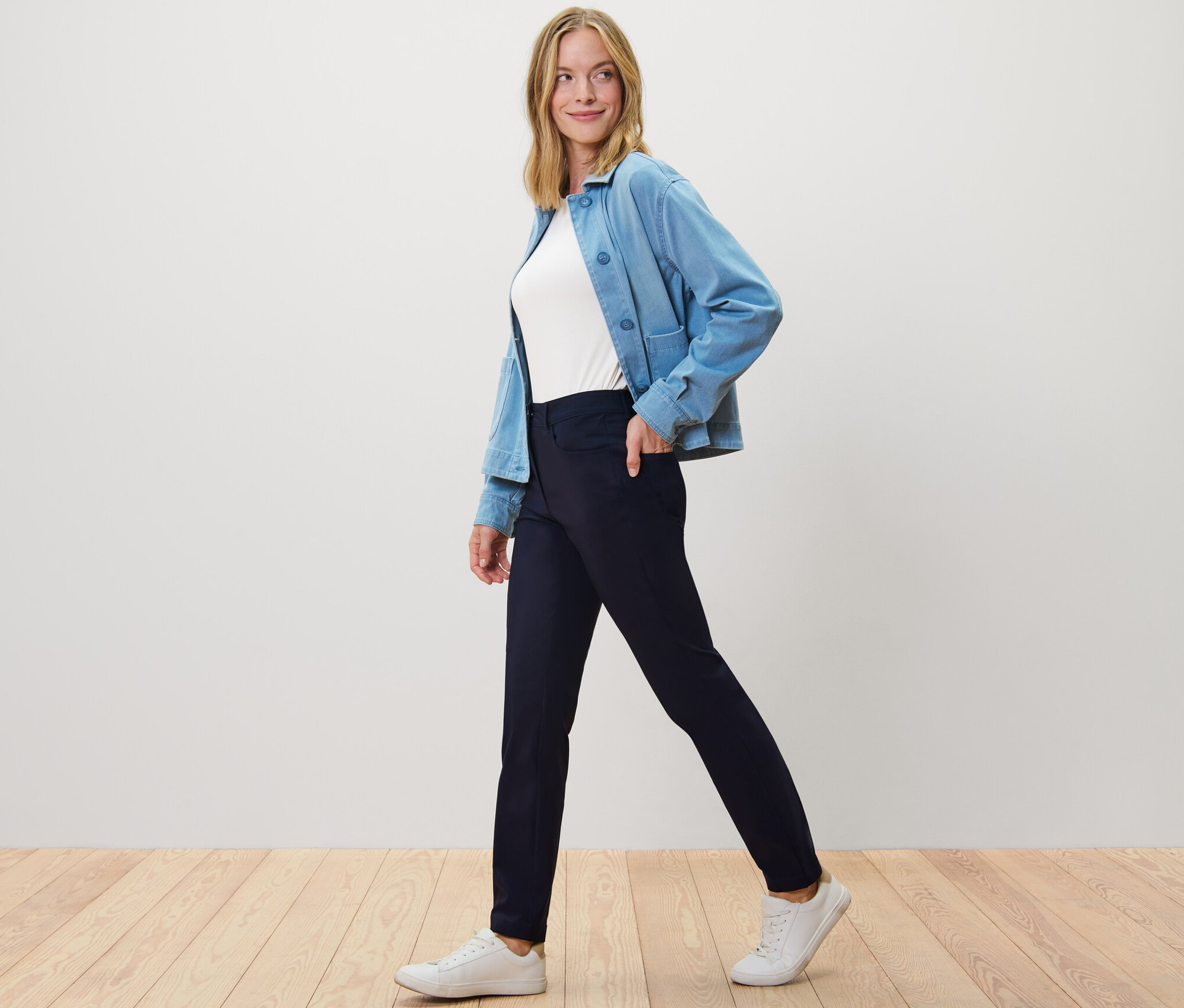 Une femme marche et porte un pantalon en bengaline bleu foncé, un t-shirt blanc et une veste bleue.