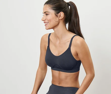 Une femme est assise sur un tabouret et porte un soutien-gorge de sport bleu sans couture.