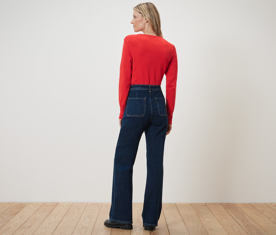 Une femme pose, le dos à la caméra, portant un jean évasé – Fit « Cara » et un haut rouge.