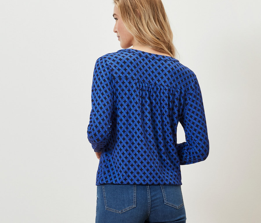Une femme porte une blouse imprimée bleu cobalt et un jean.