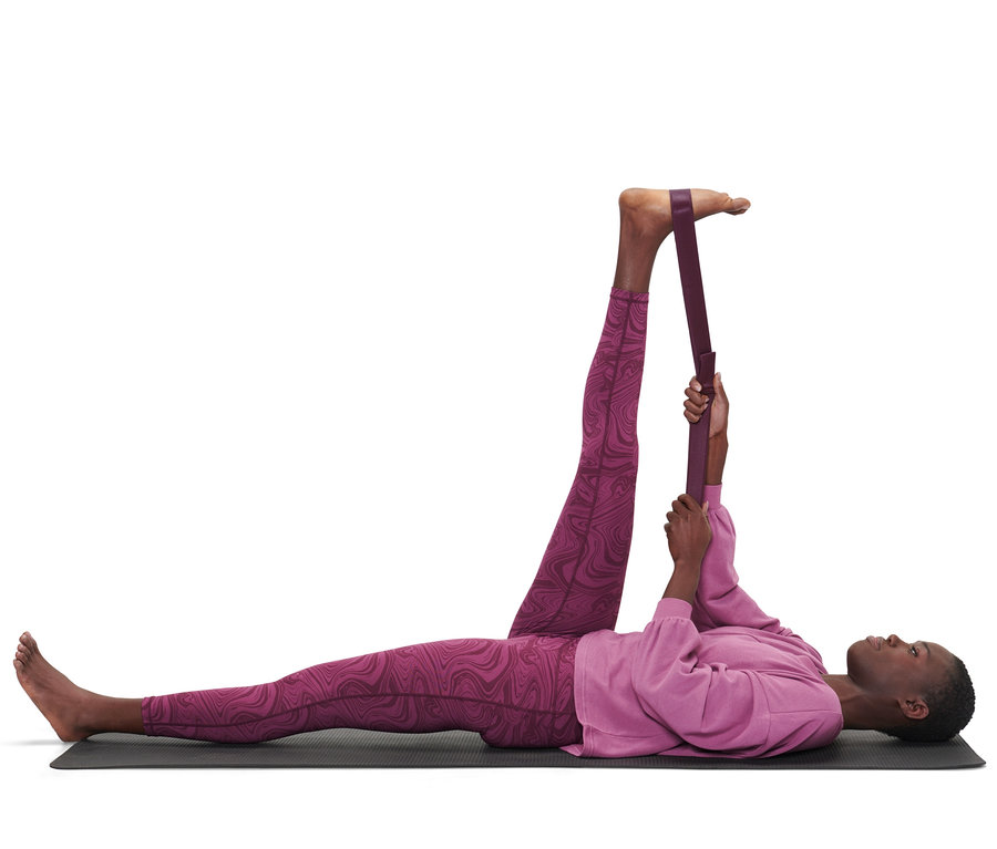 Une femme allongée sur un tapis étire sa jambe avec une ceinture de yoga 2 en 1.