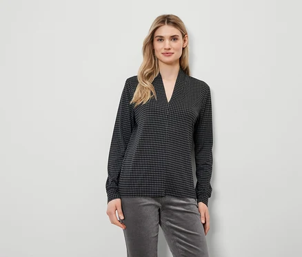 Une femme blonde porte un haut à motif pied-de-poule et un pantalon gris.