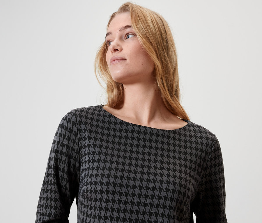 Une femme blonde aux cheveux longs porte une robe à motif pied-de-poule.