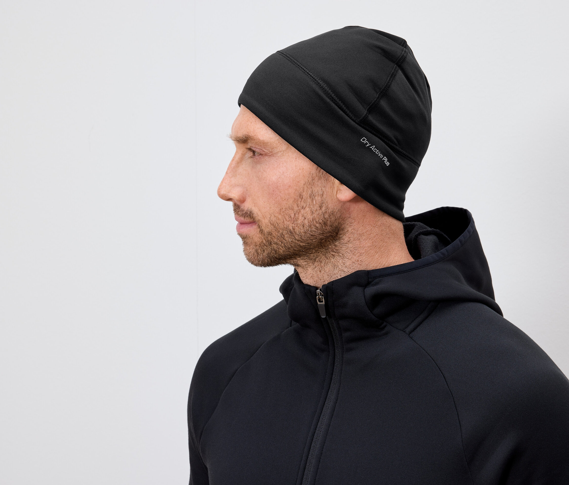 Profil d'un homme barbu portant un bonnet noir Dry Active Plus et un sweat à capuche noir.