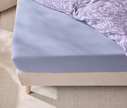 Gros plan d'un lit avec un drap-housse bleu et une literie à motifs de feuilles.