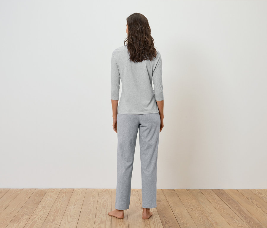 Vue de dos d'une femme aux cheveux bruns ondulés portant un t-shirt gris à manches trois-quarts et un pantalon gris.