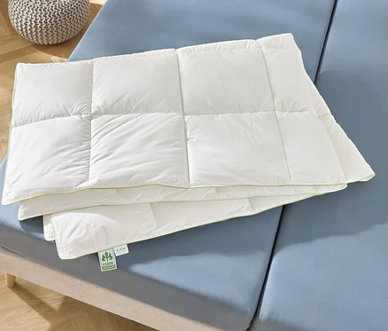 Une couette blanche pliée repose sur un lit bleu.