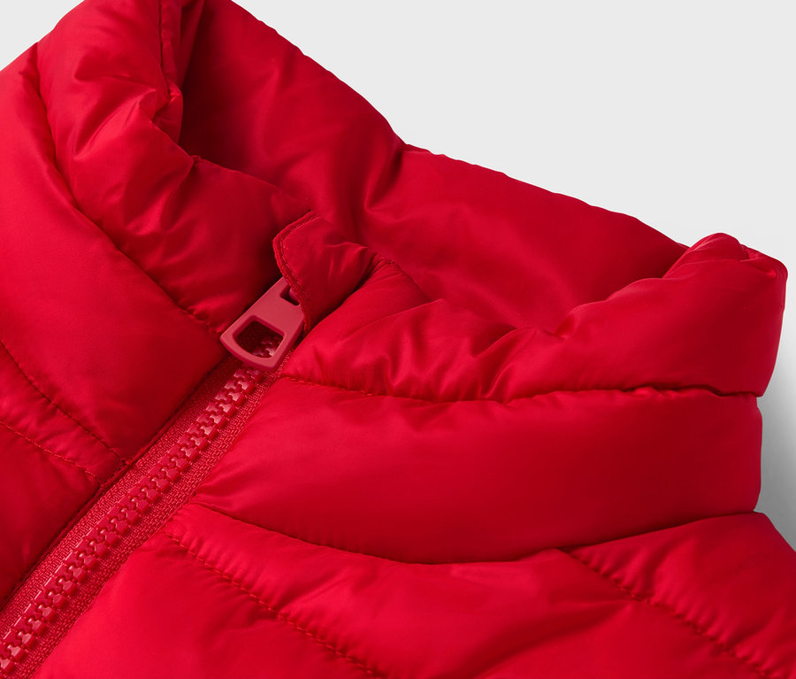 Détail d'un gilet matelassé rouge avec fermeture éclair rouge.