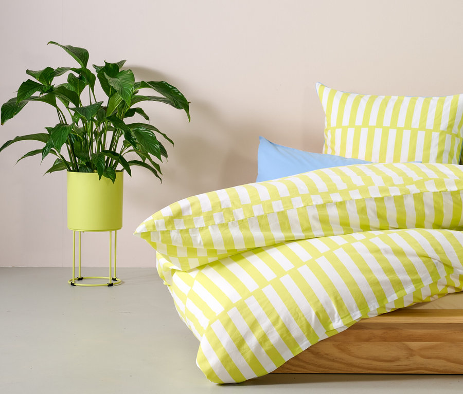 Une plante verte dans un cache-pot rond est à côté d'un lit avec des rayures jaunes.