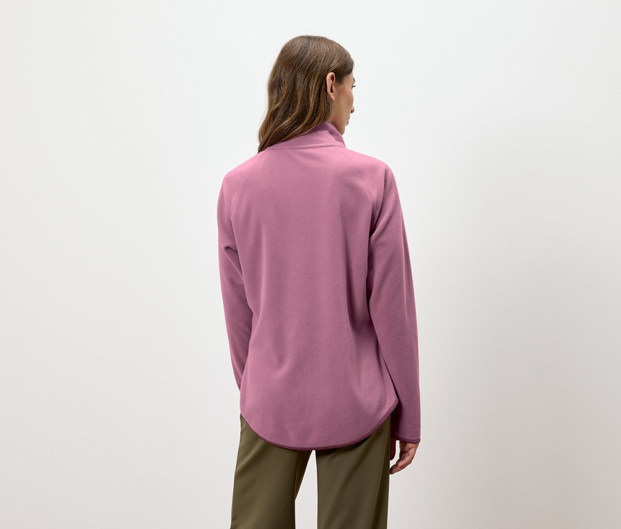 Une femme, vue de dos, porte un pull en polaire rose et un pantalon vert.
