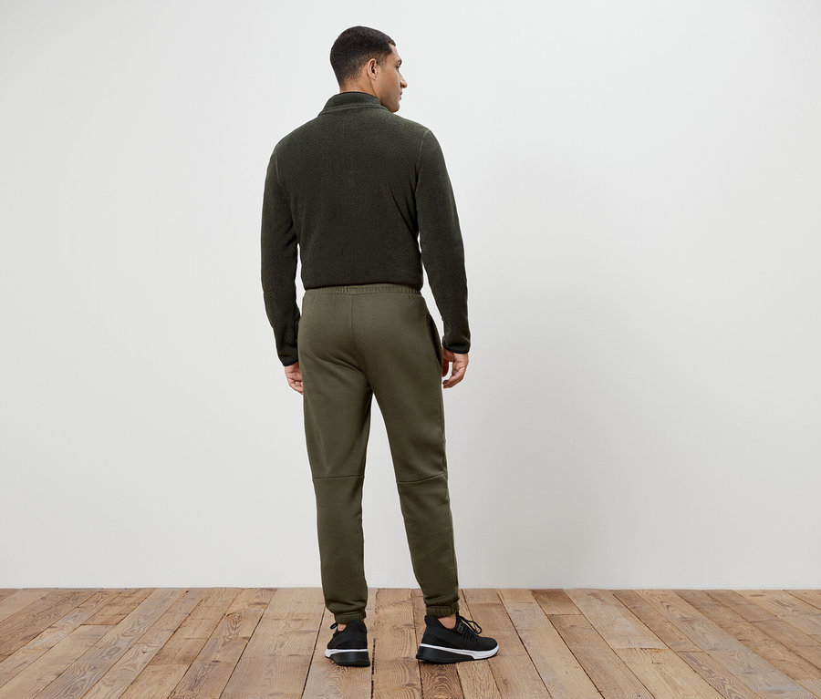 Un homme portant un pull en laine polaire vert olive et un pantalon de survêtement, dos à la caméra.