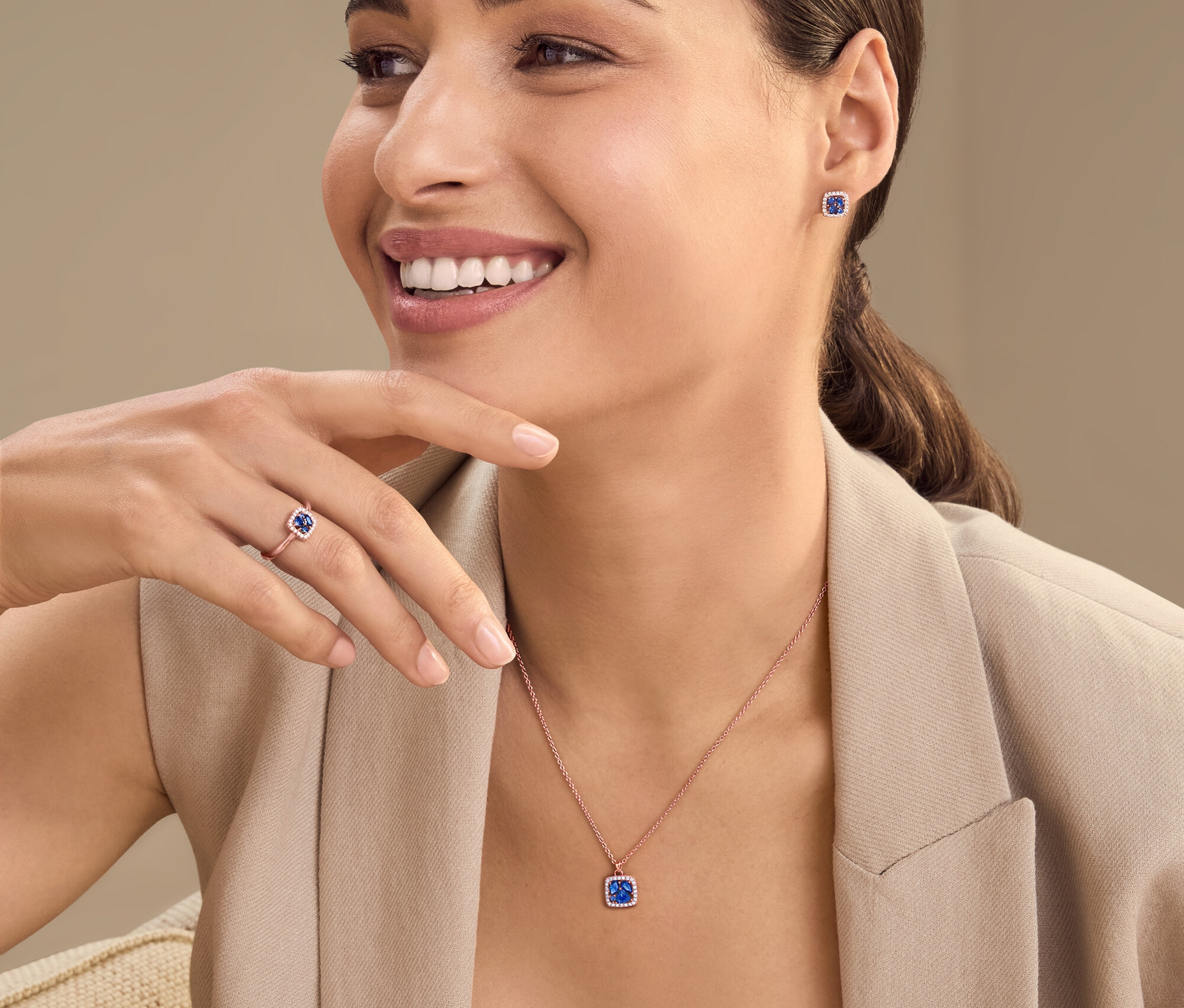 Femme souriante portant un collier, des boucles d'oreilles et une bague avec des pierres précieuses.