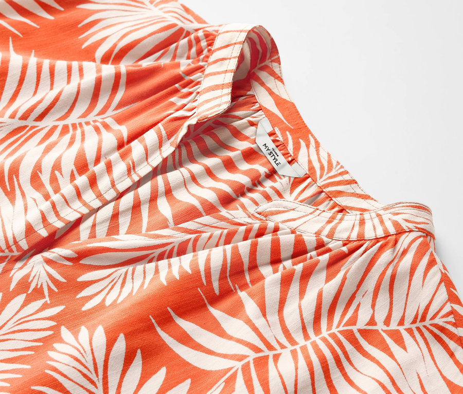 Gros plan sur un chemisier imprimé à manches courtes orange avec des motifs de feuilles.