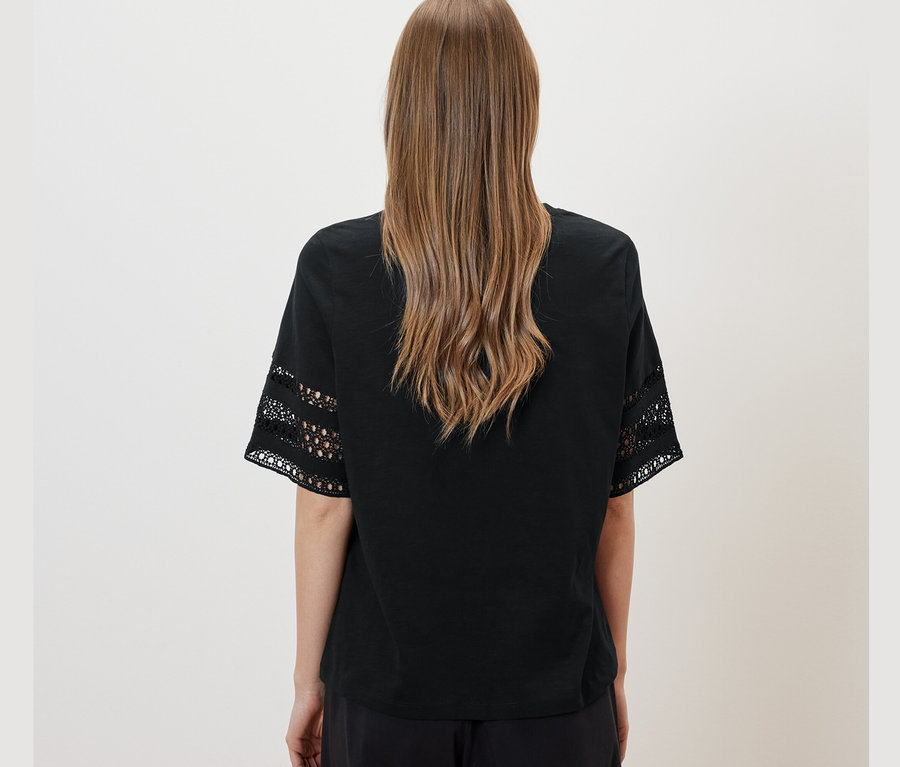 Vue arrière d'une femme aux cheveux bruns portant un t-shirt à broderie noir et un pantalon noir.