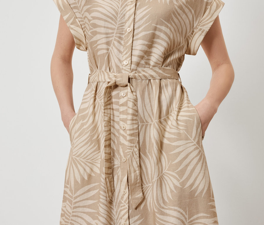 Femme posant dans une robe en lin imprimée avec un motif de feuilles, les mains dans les poches.