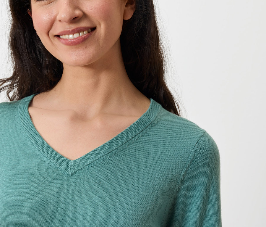 Portrait d'une femme souriante portant un pull turquoise à col en V.