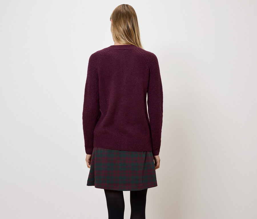 Femme vue de dos portant un pull bordeaux et une jupe à carreaux.