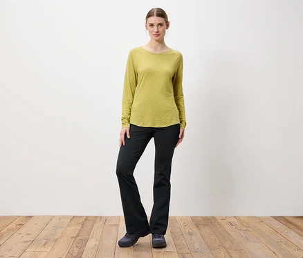 Une femme pose en chemise à manches longues vert clair et pantalon noir.