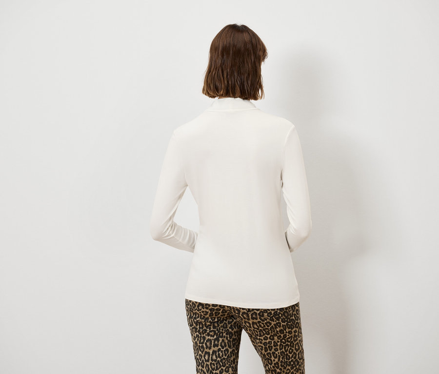 Vue arrière d'une femme aux cheveux bruns portant un haut à manches longues couleur crème et un pantalon léopard.