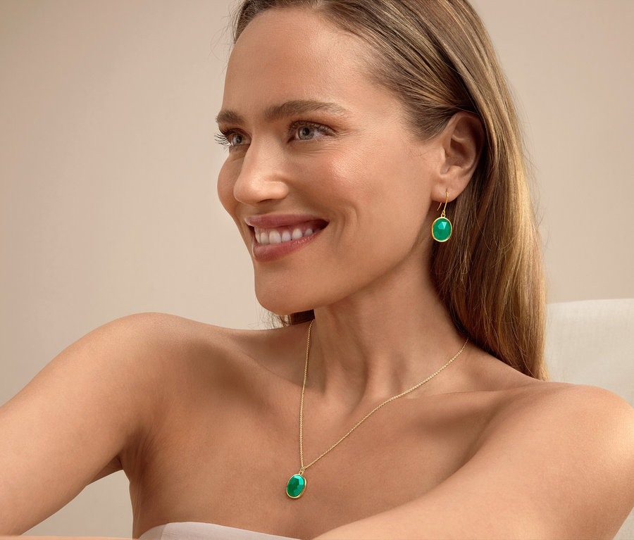 Femme souriante aux cheveux blonds portant des boucles d'oreilles et un collier verts.