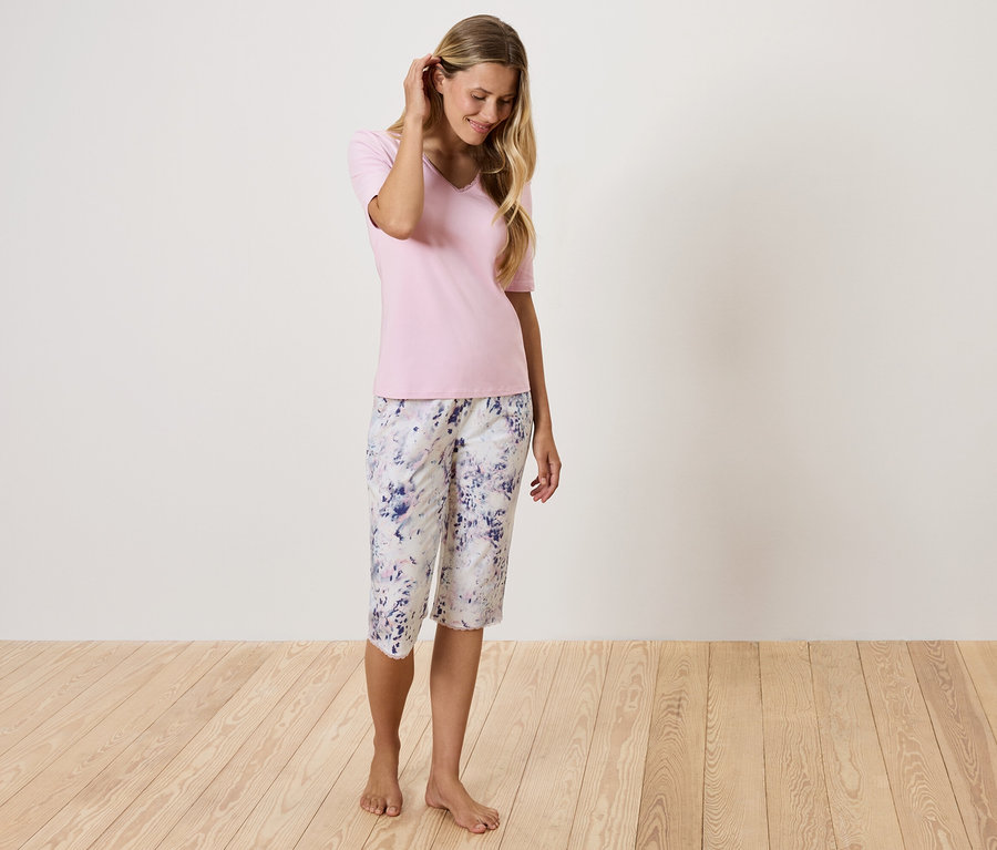 Femme en T-shirt rose et pantalon à fleurs debout sur un plancher en bois.